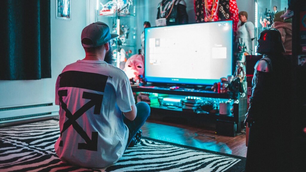 A man wearing a cap sitting on a bed and playing a game. 