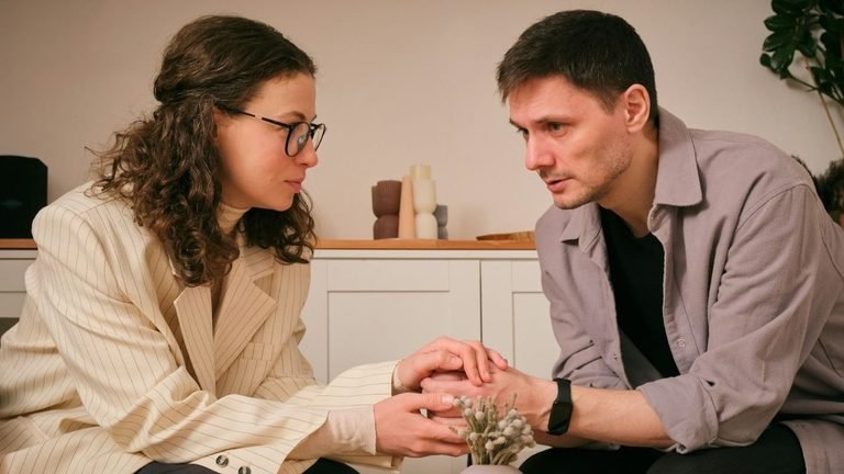A man and a woman standing face-to-face, holding hands and looking serious.