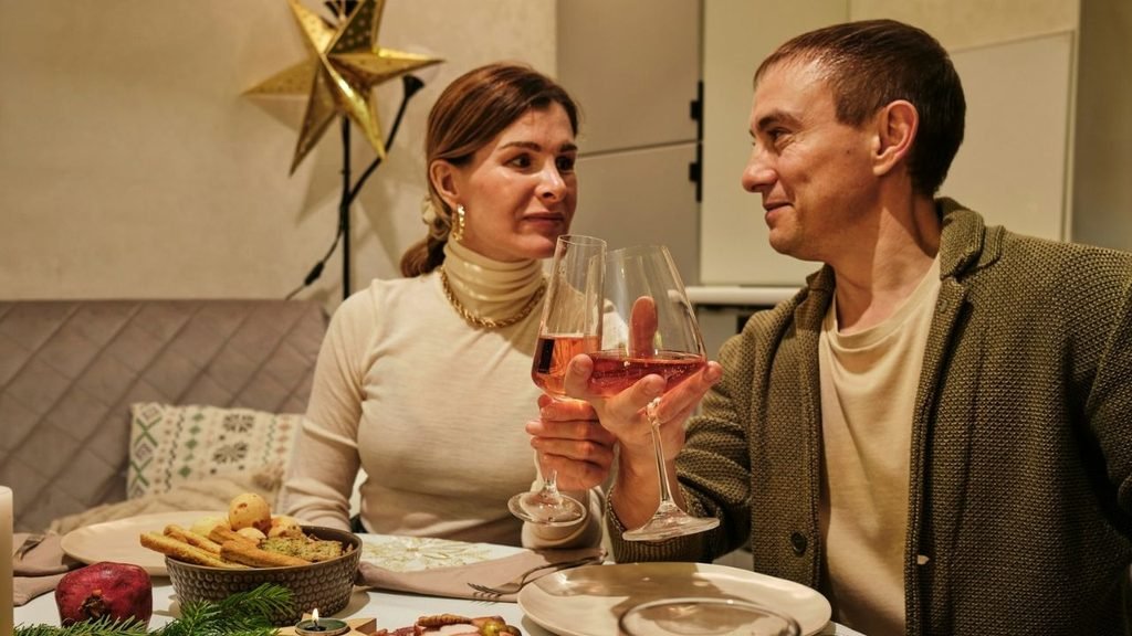 Man and woman at a dinner table toasting with glasses of rose-colored wine.