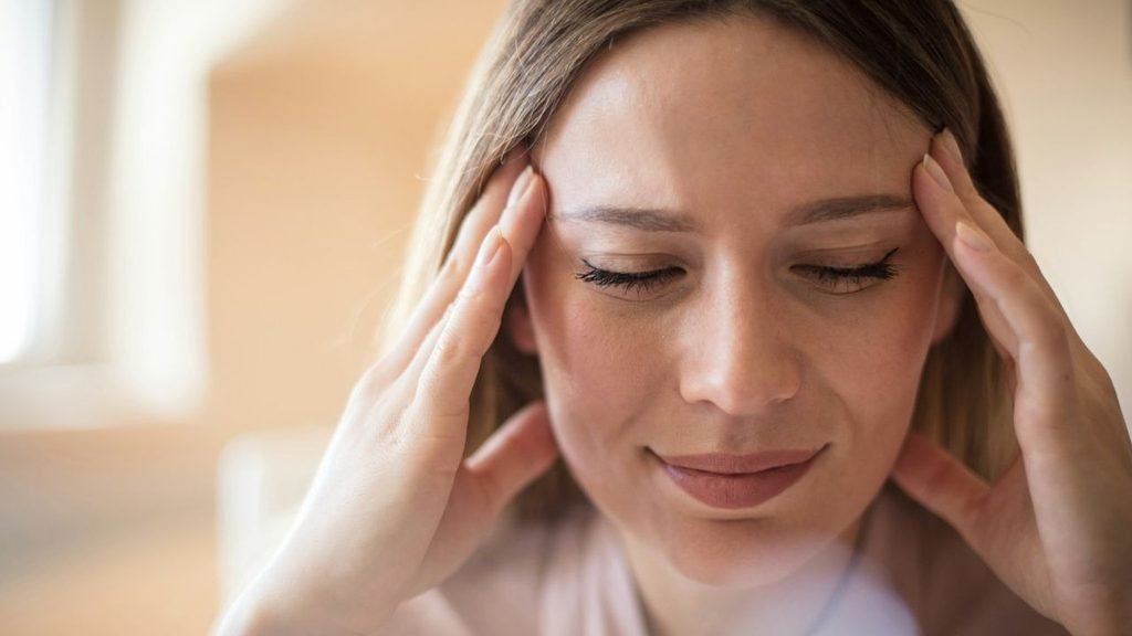 A woman pressing her palms to her temples with her eyes closed in a room.