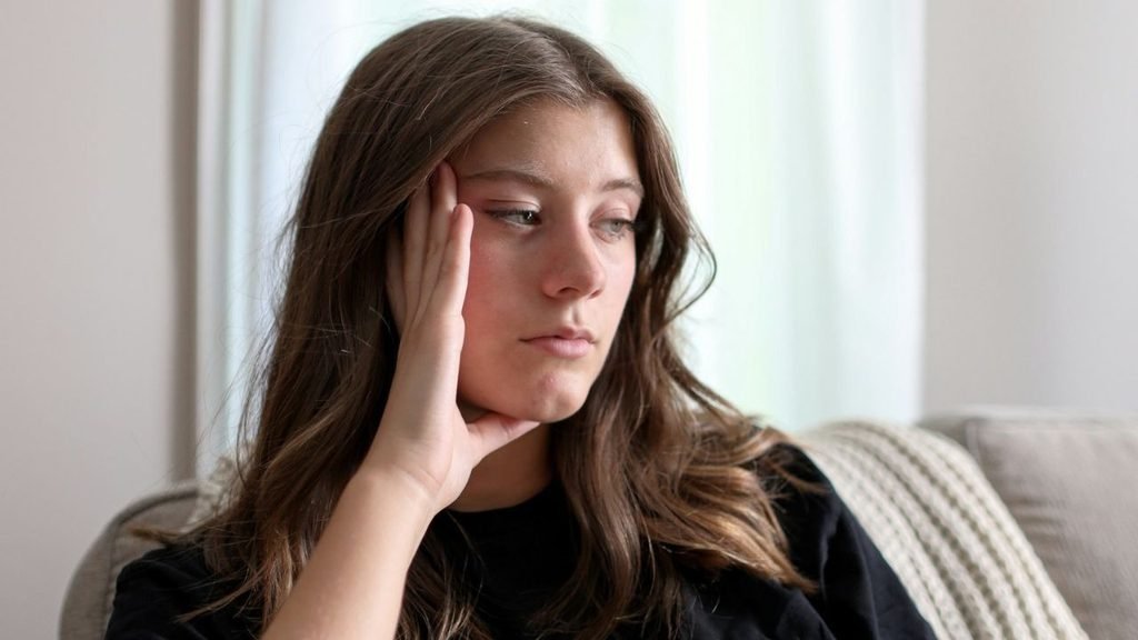 Young woman with brown hair, resting her head on her hand, looking away, indoors.