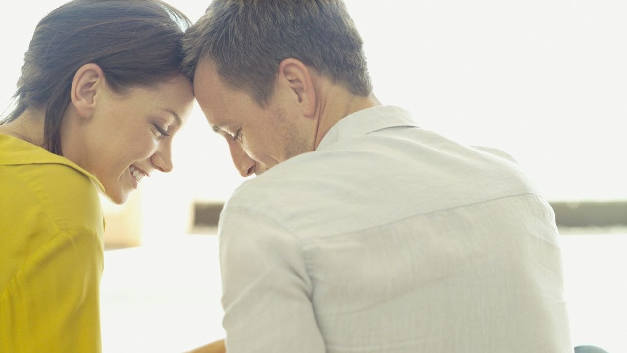 Man and woman leaning their foreheads together, the woman smiling, in a bright setting.