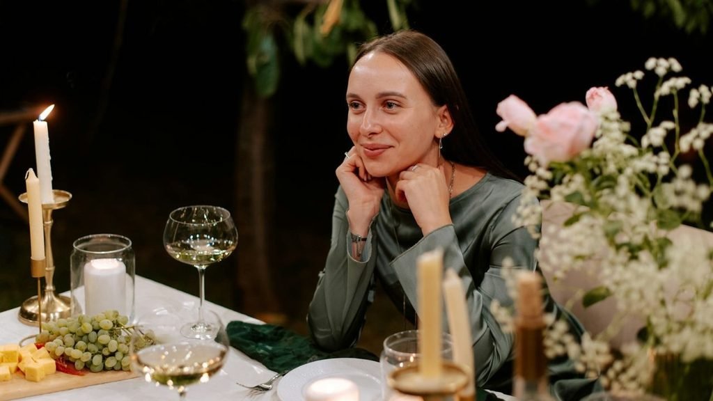 Smiling woman with her chin resting on her hands at a candlelit outdoor dinner table.
