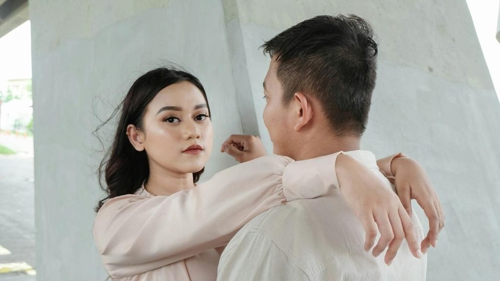 A woman with an intense expression has her arms wrapped around a man's neck as she looks directly at the camera.