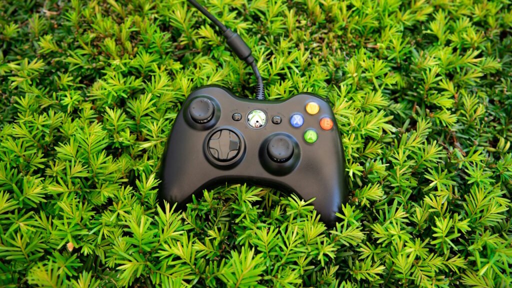 An Xbox 360 Controller lying on top of green grass. 